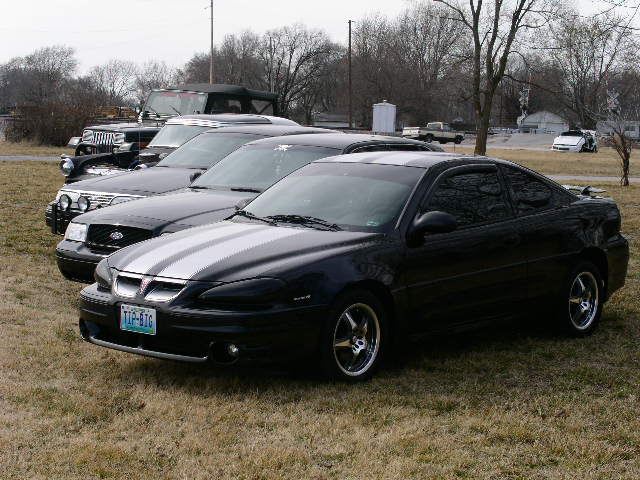 Black coupe with silver racing stripes parked in a lot with other vehicles