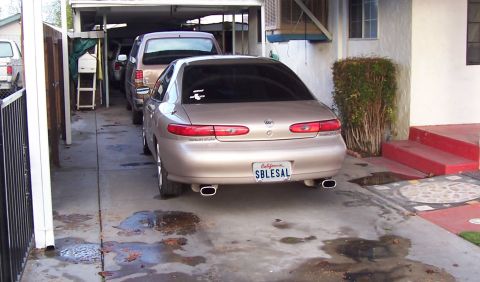 1993 Ford Taurus - Rear view of a gold sedan parked in a driveway, with another vehicle behind it.