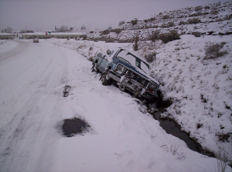 Wrecked light-blue pickup truck nose-down in a snowy roadside ditch