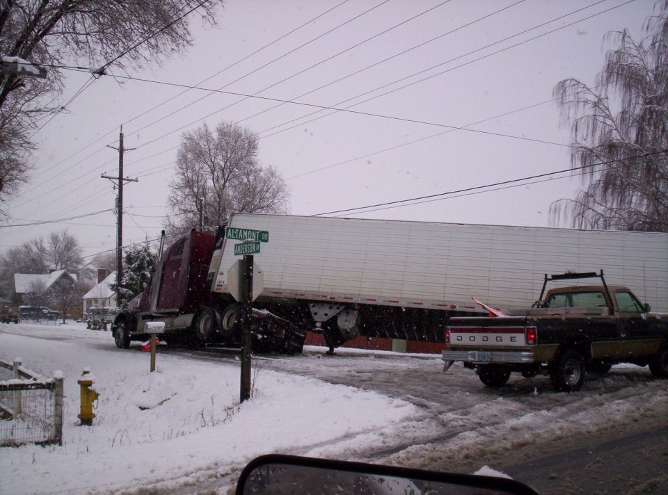 Jackknifed red semi truck with white trailer in snow, a Dodge pickup passing nearby
