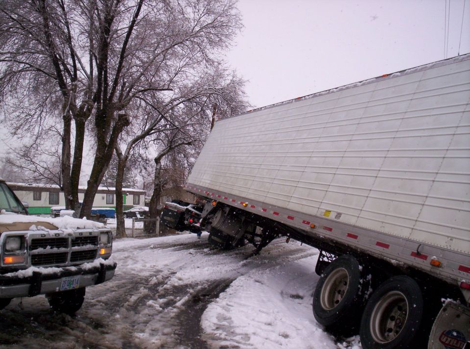 White semi trailer slid off an icy road into trees with a box truck stuck behind it