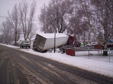 1984 Ford Bronco - A semi-trailer truck is stuck at an angle in the snow, with a pickup truck visible on the side of the road.