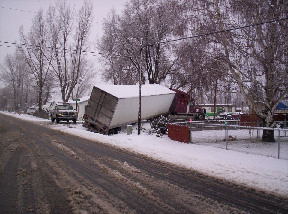 Semi-trailer truck stuck at an angle in snow, with a pickup truck nearby