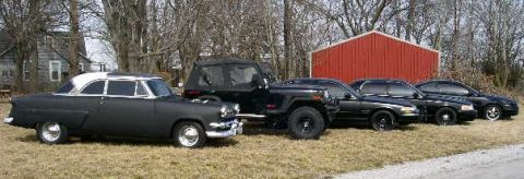 2001 Ford Crown Victoria - A collection of vehicles, including a Jeep and several sedans, are parked outdoors near a rural building.