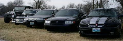 2001 Ford Crown Victoria - A collection of vehicles, including a Jeep, a Ford Crown Victoria, and a Pontiac GTO, are lined up outdoors.