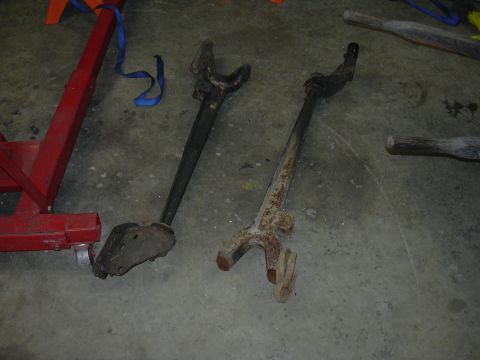 1991 Ford Bronco - Close-up of two worn and rusty vehicle suspension parts resting on a garage floor.