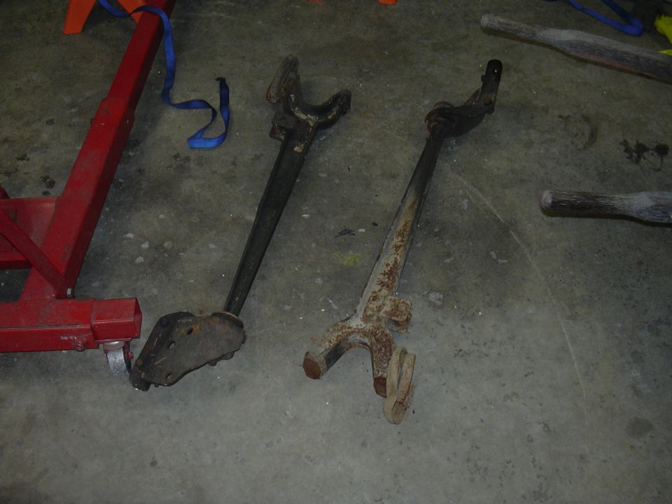 Two rusty automotive suspension components on a concrete floor next to a red engine hoist