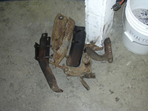 1991 Ford Bronco - A collection of various rusty metal components are scattered on a concrete surface, next to a white bucket with writing on it.