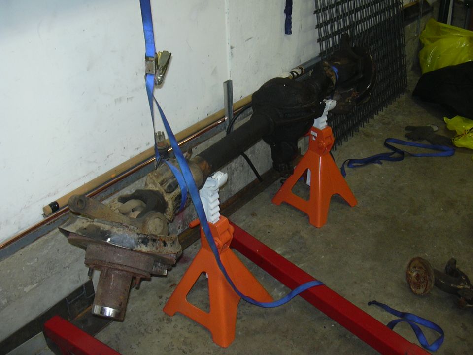 Vehicle axle assembly supported by orange jack stands, secured with blue straps