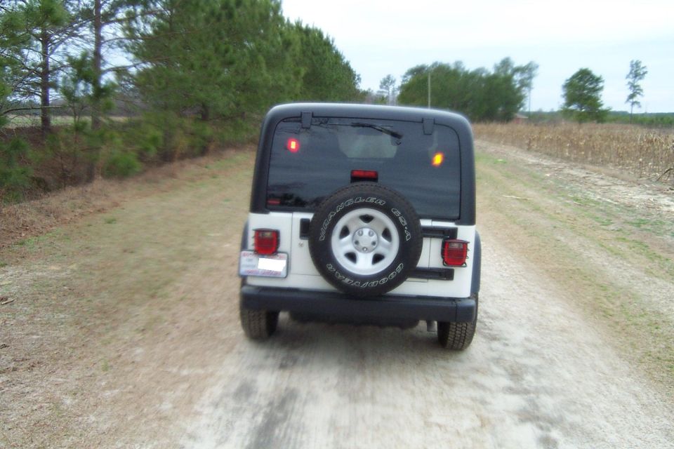 Rear view of a white 2006 Jeep Wrangler on a dirt road