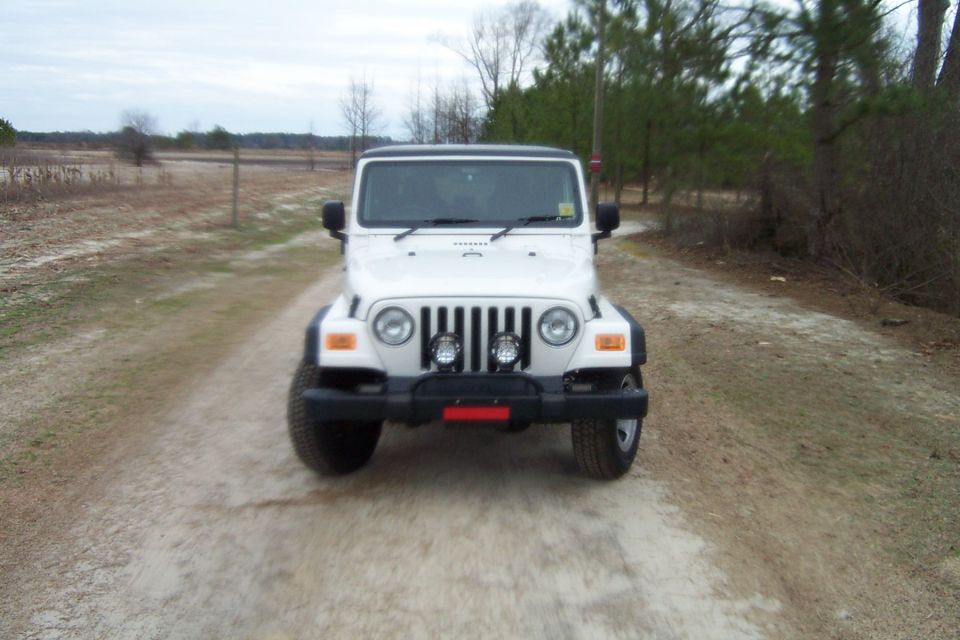 White 2006 Jeep Wrangler front view on a dirt road with trees in the background
