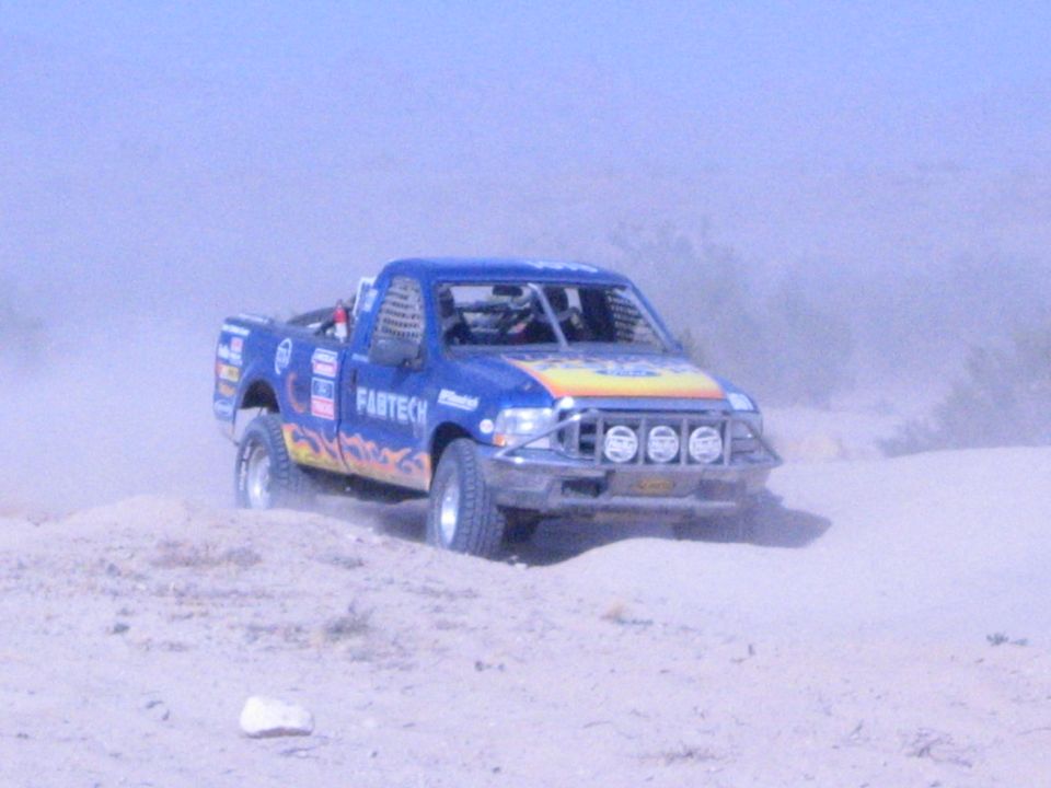 Blue Fabtech off-road race truck with flames racing across sandy desert wash