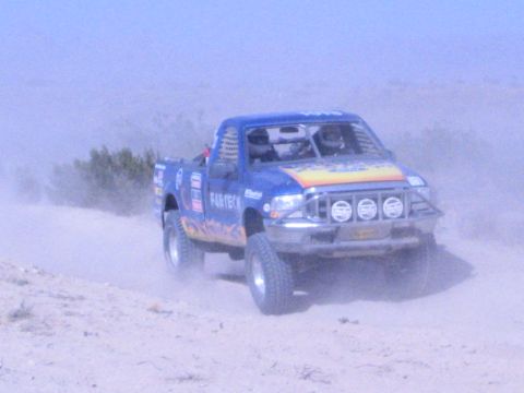 Blue flamed off-road race truck with four front lights powering through desert dust