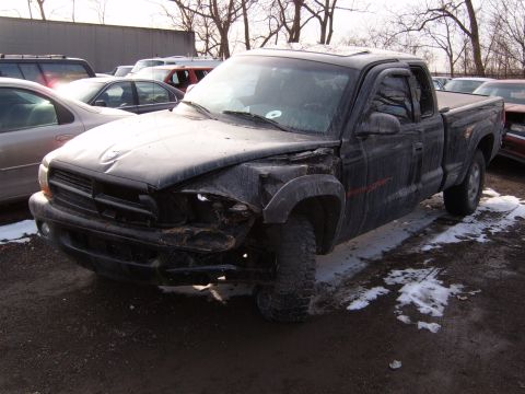 1993 Ford Bronco - A damaged black pickup truck sits in a lot, surrounded by other vehicles and patches of snow.