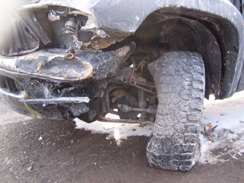 1993 Ford Bronco - The front end of a vehicle is severely damaged, with a flat tire and exposed mechanical components visible.