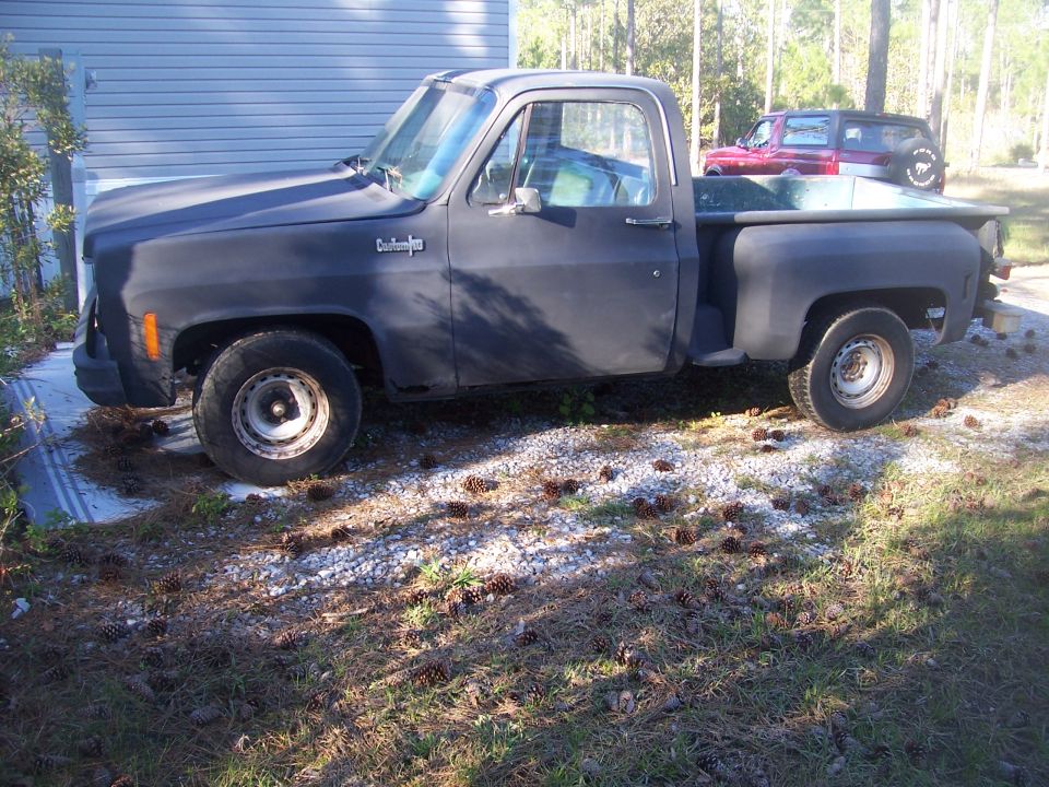 Side view of a dark-colored Chevrolet pickup truck parked outside. Another SUV is visible in the background