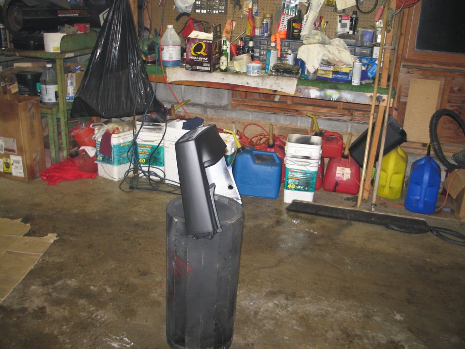 Black and silver plastic body panel propped on a drum in a cluttered home garage