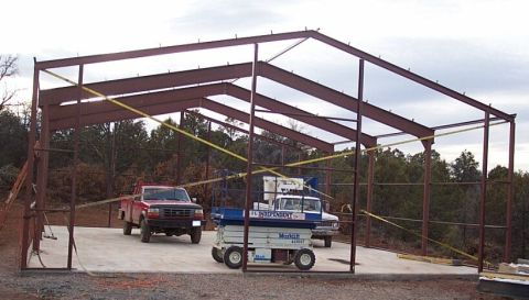 1986 Ford Ranger - A red pickup truck and a blue scissor lift are parked inside a metal building under construction.