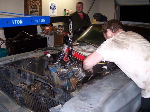 1967 Ford Mustang - Two men work on removing the engine from a 1967 Ford Mustang in a garage.