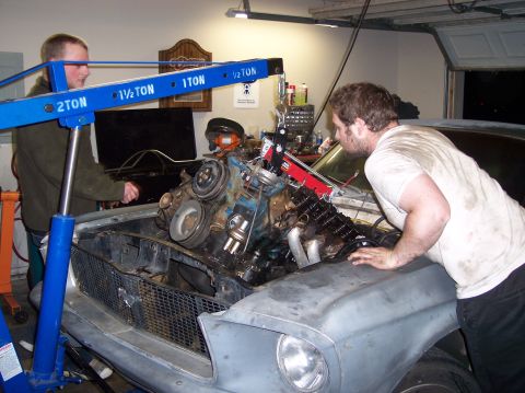 1967 Ford Mustang - Mechanics use an engine hoist to remove the engine from a 1967 Ford Mustang in a garage.