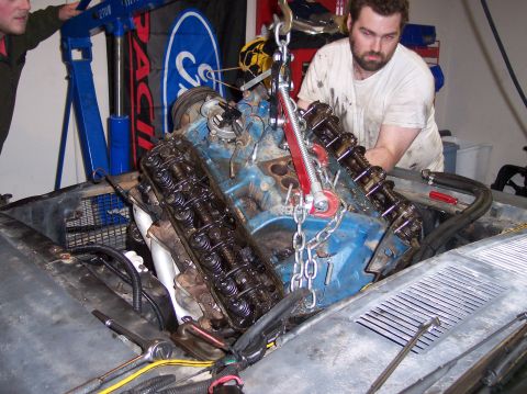 1967 Ford Mustang - Mechanics are removing an engine from a vehicle using an engine hoist in a garage setting.