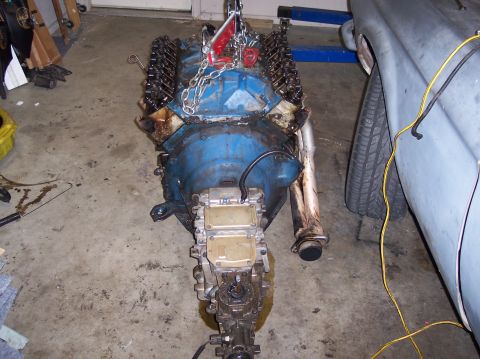 1967 Ford Mustang - Engine removed from a vehicle, showing the blue block and exhaust system, with a portion of the car visible on the right.