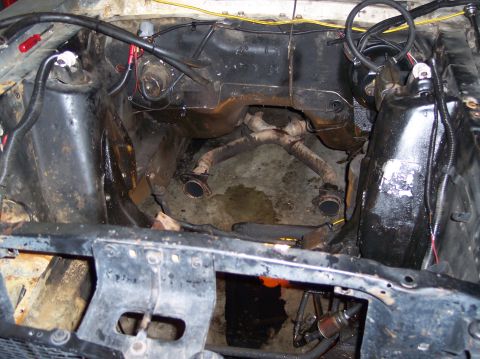 1967 Ford Mustang - The engine bay of a vehicle, showing the exhaust system and various hoses and wiring.