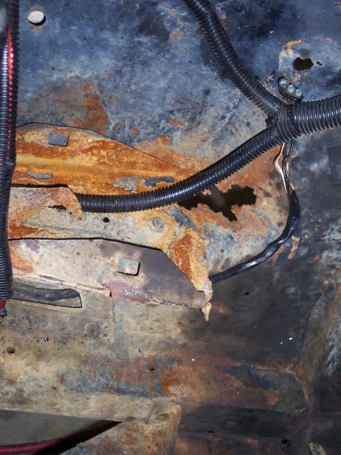 1967 Ford Mustang - Close-up of heavily rusted vehicle frame components with black wiring conduits visible.