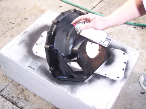 1967 Ford Mustang - A hand sprays black paint onto a metal automotive part resting on a white box.