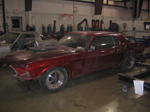 1969 Ford Mustang - A red 1969 Ford Mustang coupe sits in a workshop, appearing to be undergoing modifications.