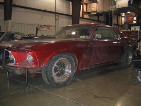 1969 Ford Mustang - This 1969 Ford Mustang coupe is in a workshop, showing its red paint and hood scoop.