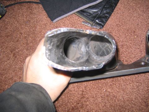 1969 Ford Mustang - Close-up of a metal exhaust manifold part, held by a hand.