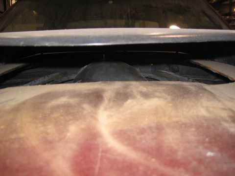 1969 Ford Mustang - A view of the hood scoop opening on a vehicle, showing a dark rubber seal and a red body panel underneath.