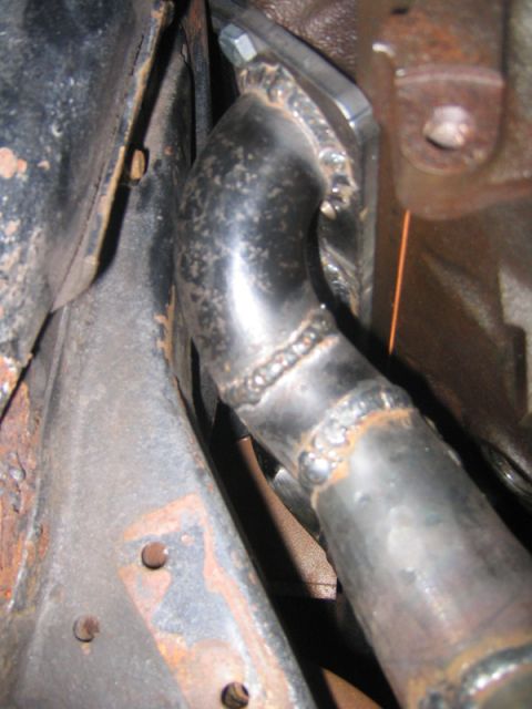 1969 Ford Mustang - This image shows a close-up view of a custom exhaust pipe connection, visible welds and some rust on the surrounding chassis components.