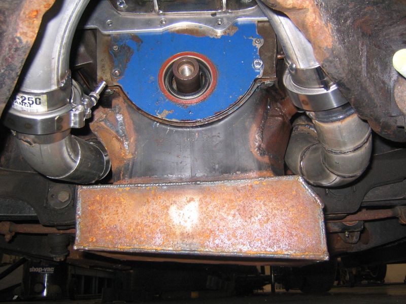 Engine block with blue plate, red seal, and stainless steel pipes. Rusty metal shield below