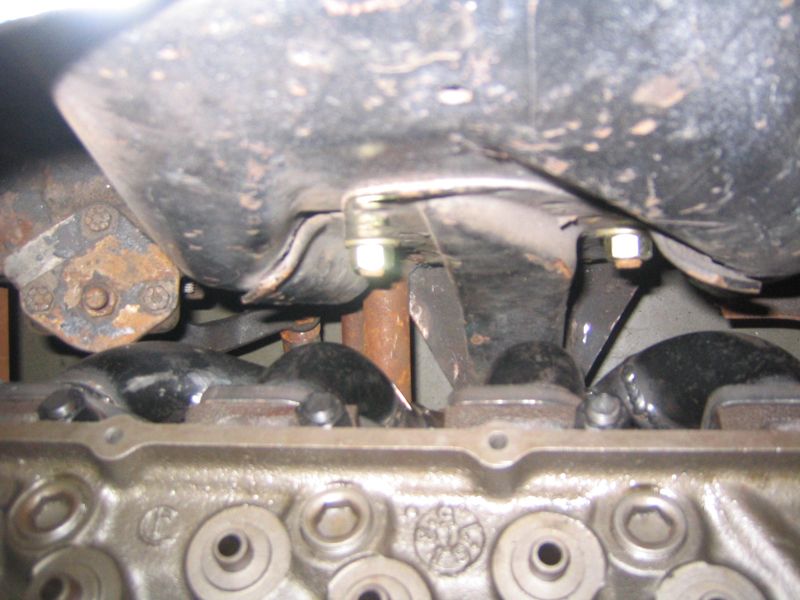 Close-up of an engine block with the oil pan above it. Bolts and rusty metal parts are visible