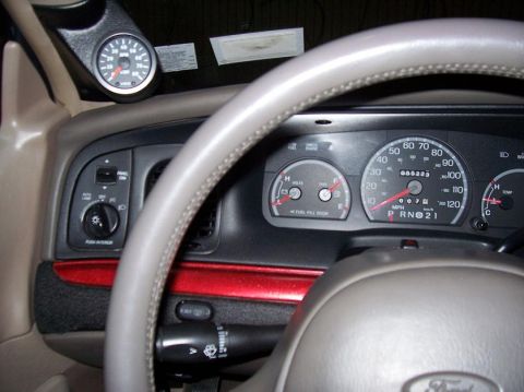 1999 Ford Crown Victoria - The interior of a 1999 Ford Crown Victoria shows the dashboard, steering wheel, and an aftermarket gauge, with the odometer displaying 55,2…