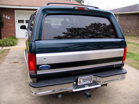 1995 Ford C-150 (Centurion Conversions) - The rear of a Ford truck, likely from the mid-1990s, is parked in a driveway next to a brick house.