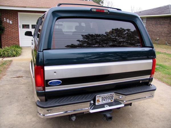 Rear view of a dark green Ford F-Series truck with a silver stripe and a camper shell. License plate reads B0990R
