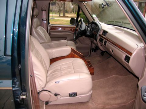 1995 Ford C-150 (Centurion Conversions) - Interior view of a van with captain's chairs and wood trim.