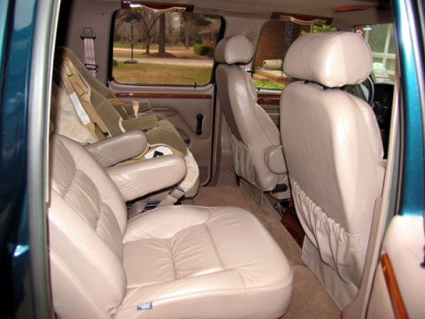 1995 Ford C-150 (Centurion Conversions) - Van interior with multiple rows of tan leather seats and child seat installed.