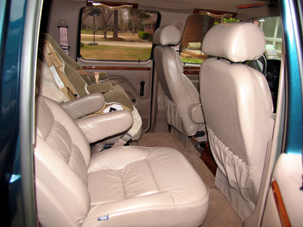 Tan leather captain's chairs and wood trim in the rear cabin of a teal conversion truck