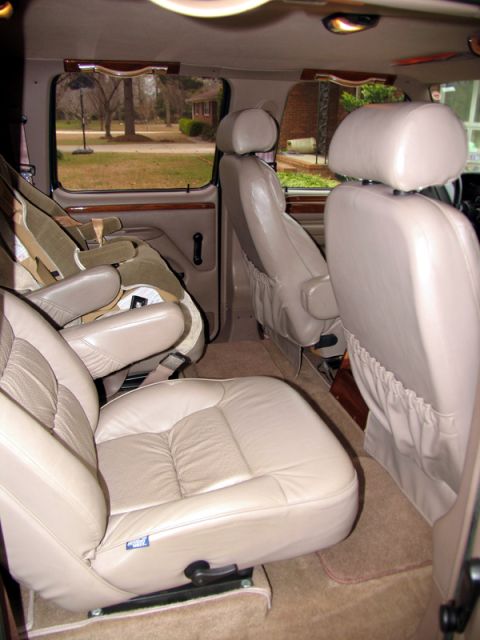 1995 Ford C-150 (Centurion Conversions) - The interior of a van is shown, multiple rows of tan leather seats and a child seat installed.