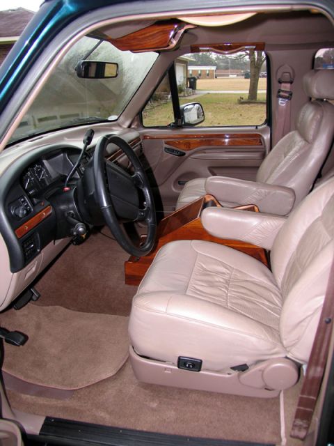 1995 Ford C-150 (Centurion Conversions) - The interior of a van features tan leather captain's chairs and wood accents on the dashboard and doors.