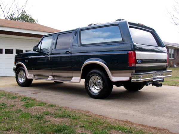 Teal and tan four-door Ford Bronco conversion SUV, rear three-quarter view in driveway