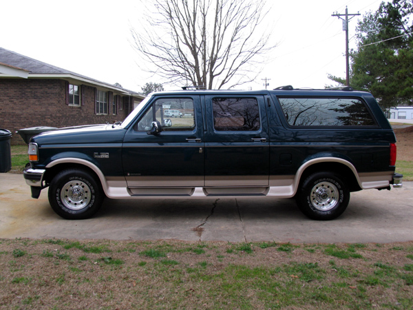 Dark green four-door Ford Bronco conversion SUV with tan two-tone trim, side view in driveway