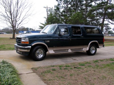 1995 Ford C-150 (Centurion Conversions) - A dark green Ford Bronco Centurion Conversion is parked on a concrete driveway with grass and trees in the background.