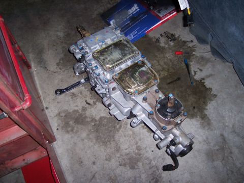 1967 Ford Mustang - A manual transmission is shown disassembled on a garage floor, with tools and parts scattered around.
