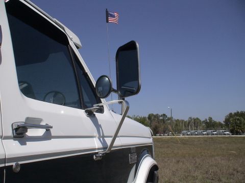 1993 Ford C-350 (Centurion Conversions) - Close-up of a truck's side door and towing mirrors, with an American flag flying against a clear blue sky.