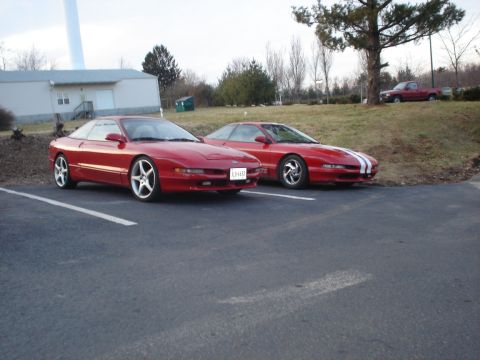 1993 Ford Probe - Two red 1993 Ford Probes are parked in a lot. One has racing stripes.